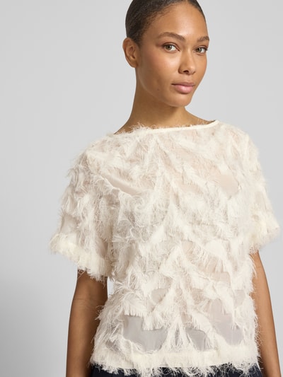 Kobieta modelka nosi Relaxed Fit Bluse mit Fransen Modell 'MYLINE' od Selected Femme, kremowa, jednolita, półprzezroczyste wykończenie, krótki rękaw, dekolt łódka, krój relaxed fit, z frędzlami, zbliżenie na górną część ciała