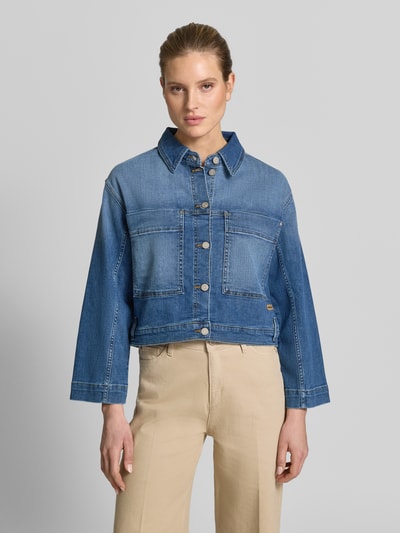 Modelka kobieca nosi Jeansjacke im Used-Look mit Label-Detail Modell 'Tina' od Gang, bawełna z domieszką elastyczną, krój relaxed fit, używany wygląd, niebieska, kontrastowe szwy, kieszenie na piersi, detal z logo, długość tyłu w rozmiarze S 54 cm, szerokość ramion w rozmiarze S 49 cm, szerokość w biuście w rozmiarze S 46 cm, długość rękawa w rozmiarze S 54 cm, widok całej sylwetki z przodu.