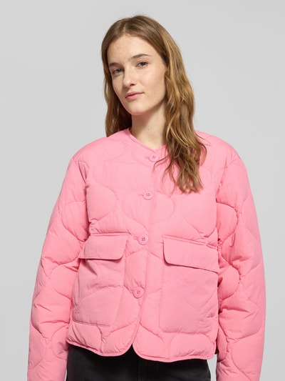 Modelka kobieca ma na sobie różową, pikowaną steppjacke z guzikami Steppjacke mit Knopfleiste Modell 'HOPE' od JJXX, prosty krój, okrągły dekolt, kieszenie z patką, długość tyłu w rozmiarze S: 56 cm, szerokość ramion w rozmiarze S: 45 cm, szerokość w rozmiarze S: 51 cm, długość rękawa w rozmiarze S: 56 cm, tekstura matowa, ujęcie: zbliżenie na górną część ciała z przodu.