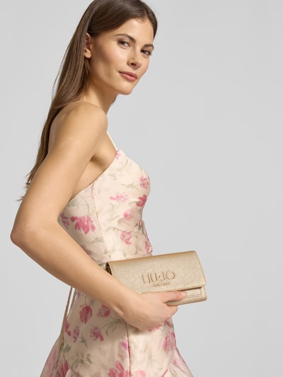 Frauenmodel trägt Portemonnaie mit Logo-Prägung von Liu Jo White in Beige mit feiner Textur, Überschlag und Magnetverschluss, Nahaufnahme Oberkörper.