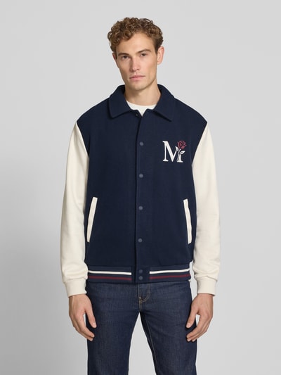 Männermodel trägt Regular Fit jack met motiefstitching van MCNEAL in marineblauw en gebroken wit, platte kraag, knoopsluiting, elastische boordjes, ruglengte maat M 68 cm, mouwlengte maat M 68 cm, volledige lichaamsaanzicht van voren.