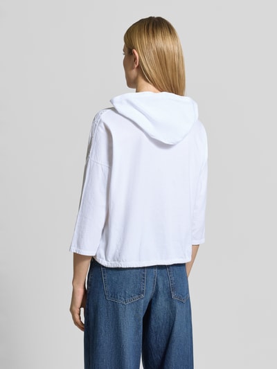 Frauenmodel trägt Bluse mit Kapuze Modell 'Is4aa' von ZABAIONE, Reine Baumwolle, Gerader-Schnitt, Lochstickerei, Ganzkörperansicht Rückansicht.