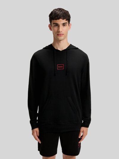 Männermodel trägt Regular Fit Hoodie aus Baumwoll-Mix Modell 'LAZE' von HUGO in Schwarz mit Label Print und Kängurutasche, Ganzkörperansicht von vorne.