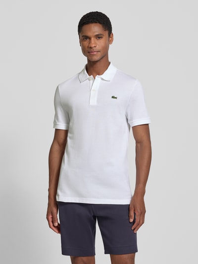 Männermodel trägt Slim Fit Poloshirt aus reiner Baumwolle von Lacoste in Weiß, glatte Struktur, kurze Ärmel, Ganzkörperansicht von vorne.