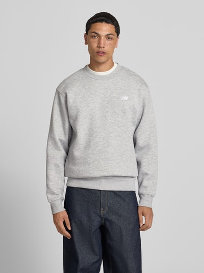 Männermodel trägt Sweatshirt mit Rundhalsausschnitt und Label-Stitching von New Balance aus Baumwoll-Mix, Farbe Hellgrau, Relaxed-Fit, Ganzkörperansicht von vorne. Rückenlänge 67 cm, Ärmellänge 63 cm bei Größe M.