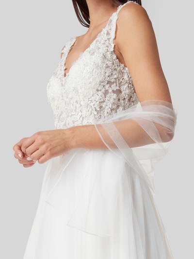 Kobiece model prezentuje Brautkleid mit Ziersteinen und floraler Spitze od Mascara, taliowany krój, dekolt w serek, szerokie ramiączka, koronka kwiatowa, ozdobne kamienie, półprzezroczysty materiał wierzchni, halka pod sukienkę, zapięcie na haftkę i wszyty zamek błyskawiczny, długość tyłu w rozmiarze 36: 150 cm, szerokość klatki piersiowej w rozmiarze 36: 39 cm, zbliżenie na górną część sukienki