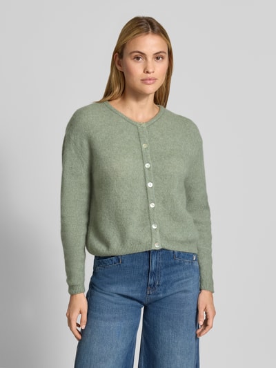 Frauenmodel trägt Relaxed Fit Strickjacke aus Woll-Mix mit Leinen-Anteil von American Vintage, hellgrün, gerippte Bündchen, Ganzkörperansicht von vorne. Damen Strickjacke, durchgehende Knopfleiste, langärmlig, Rückenlänge 52 cm, Ärmellänge 56 cm.
