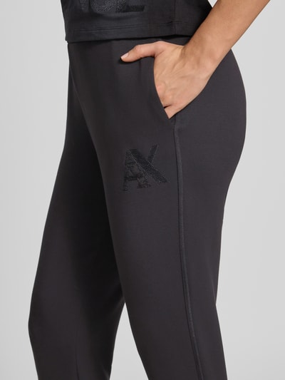 Kobiece modelka nosi Slim Fit Sweatpants aus Viskose-Mix od Armani Exchange, czarne z elastycznym pasem i wykończeniami, mieszanka wiskozy, krój slim fit, widoczna długość wewnętrzna nogawki 74 cm w rozmiarze S, detal boczny z logo AX, zbliżenie na biodro i kieszeń, zdjęcie detaliczne.