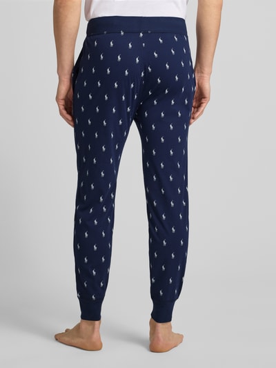 Männermodel trägt Sweathose mit Allover-Logo-Print von Polo Ralph Lauren in donkerblauw met wit logo, katoen, losse pasvorm, elastische tailleband, detailopname achterkant.