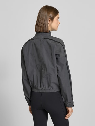 Modelka prezentuje Regular Fit Jacke mit Stehkragen od adidas Sportswear, ciemnoszara, faktura gładka, krój regular fit, długość pleców w rozmiarze S: 54 cm, szerokość ramion w rozmiarze S: 64 cm, szerokość klatki piersiowej w rozmiarze S: 64 cm, długość rękawa w rozmiarze S: 48 cm, widok całej sylwetki od tyłu.