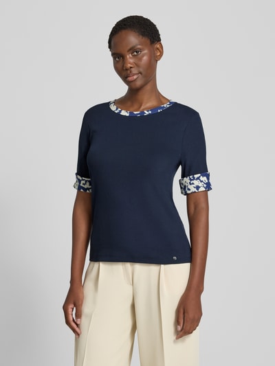 Frauenmodel trägt T-Shirt mit Rundhalsausschnitt und Ärmeln mit Aufschlag von Marc Cain in Dunkelblau, Slim Fit, Ganzkörperansicht von vorne. Baumwoll-Elasthan-Mix, kontrastierende Details an Kragen und Ärmeln, Label-Detail, Rückenlänge bei Größe 36: 54 cm.