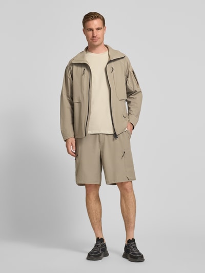 Mannenmodel draagt Relaxed Fit Cargoshorts met label-opschrift model 'GLOBE CARGO' van BOSS Green, effen beige, knoop- en ritssluiting, elastische taille, achterzak, steekzakken, ritszakken, voorkant volledig zichtbaar, volledige lichaamsweergave van voren.