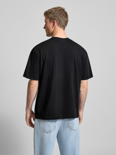 Männermodel trägt Oversized T-Shirt mit Label-Stitching von Pegador, reine Baumwolle, gerippter Rundhalsausschnitt, Rückenlänge 69 cm, Ganzkörperansicht Rückansicht.