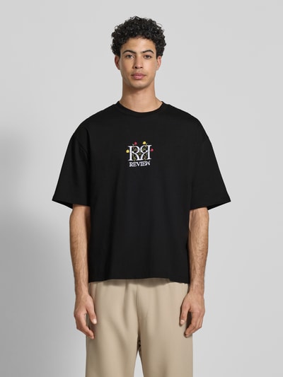 Męski model nosi Oversized Fit T-Shirt mit Logo-Stitching von REVIEW z czarnej bawełny, haftowane logo, okrągły dekolt, widok na całe ciało z przodu.