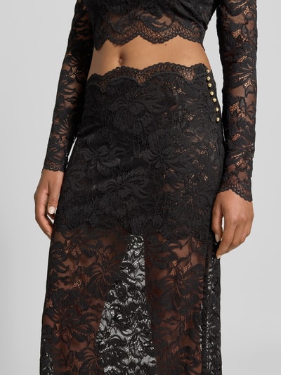 Vrouwenmodel draagt Midirok uit kant van Rabanne, zwarte elastische materiaalmix, bloemenmotief, semi-transparante look, smalle band, geschulpte zoom met kanten rand, totale lengte maat 38: 85 cm, bandwijdte maat 38: 38 cm, detailopname heup en bovenbeen.