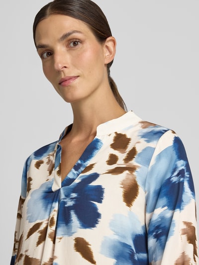 Frauenmodel trägt Relaxed Fit Bluse aus reiner Viskose Modell 'Lari' von ZABAIONE, creme mit blauen und braunen Mustern, Nahaufnahme Oberkörper. Rückenlänge 55 cm, Ärmellänge 57 cm, Serafino-Ausschnitt, langärmeliges Design.