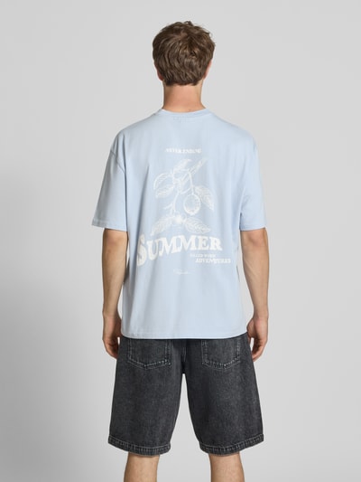 Männermodel trägt Oversized T-Shirt mit Label-Print von Pegador in Hellblau aus Reine Baumwolle, Rundhalsausschnitt, Rückenlänge 72 cm, Ganzkörperansicht Rückansicht.