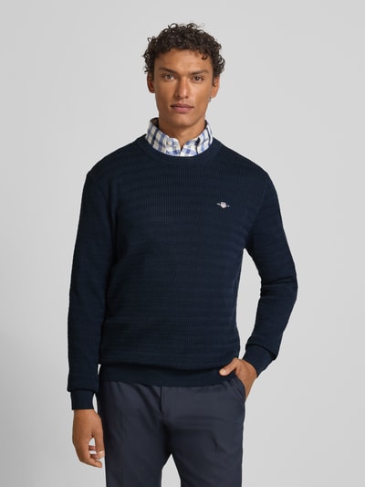 Męski model nosi Sweter z dzianiny z fakturowanym wzorem i wyhaftowanym logo od Gant, bawełna, krój regular fit, okrągły dekolt, granatowy, długość tyłu 71 cm, długość rękawa 68 cm, całkowity widok z przodu.