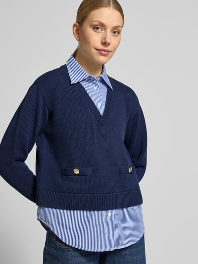 Modelka kobieca nosi Regular Fit Strickpullover aus reiner Baumwolle od Lauren Ralph Lauren w granatowym kolorze, faktura dzianiny, krój regular fit, prążkowane wykończenia, wstawka w paski, logo na aplikacji, dekolt w szpic, długi rękaw, widok na górną część ciała z przodu.