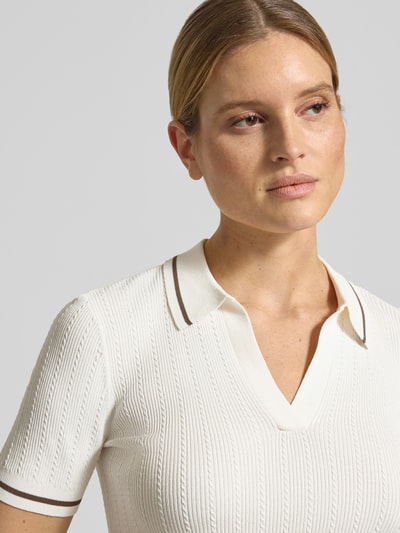 Kobiece modelka nosi Strickshirt aus Viskose-Mix mit Polokragen und V-Ausschnitt od ARMANI EXCHANGE, krój slim fit, kremowy kolor, tekstura prążkowana, z krótkim rękawem, zbliżenie górnej części ciała z przodu.