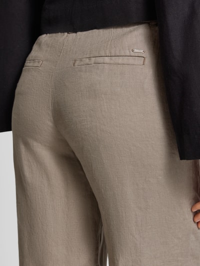 Vrouwenmodel draagt Leinenhose in verkürzter Passform van Christian Berg Woman in beige, pure linnen, paspelzakken achter, detailopname.