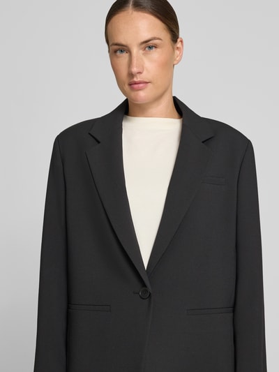 Kobiece model nosi żakiet Relaxed Fit Blazer mit Paspeltaschen Modell 'MOWTIE' od Drykorn, mieszanka materiałów z dodatkiem wiskozy, kołnierz z połami, zapięcie na guzik, kieszenie z wypustkami, długość tyłu w rozmiarze 36: 72 cm, szerokość w rozmiarze 36: 48 cm, długość rękawów w rozmiarze 36: 60 cm, kolor czarny, gładka faktura, widok z przodu, zbliżenie na górną część ciała.