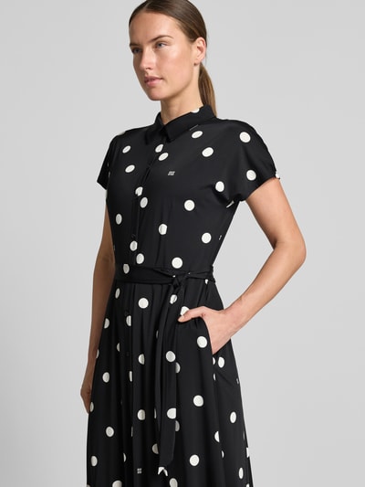 Frauenmodel trägt Hemdblusenkleid im Allover-Look mit Bindegürtel von Oui, schwarzer Stoff mit weißen Punkten, A-Linie, Nahaufnahme Oberkörper. Material-Mix mit Stretch-Anteil, Midikleid, Rückenlänge 126 cm, Brustweite 47 cm bei Größe 36.