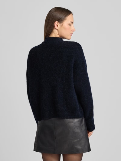 Frauenmodel trägt Regular Fit Strickjacke mit Alpaka-Anteil Modell 'Alpha' von Gestuz, elastischer Material-Mix, dunkle Farbe, Stehkragen, Rückenlänge 21 cm, Ganzkörperansicht Rückansicht.