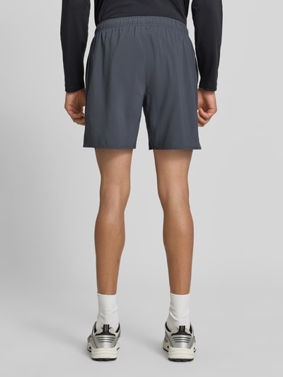 Männermodel trägt Shorts mit elastischem Bund und Logo von ASICS in Grau, lockerer Sitz, glatte Textur, Ganzkörperansicht Rückansicht. Regular Fit, elastischer Bund, Innenhose, Bundweite bei Größe M 37 cm, Innenbeinlänge bei Größe M 45 cm.