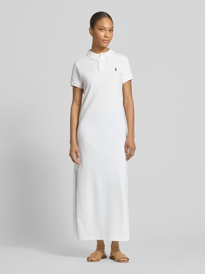 Modelka nosi Straight Fit Polokleid aus reiner Baumwolle od Polo Ralph Lauren, biała pikowana bawełna, midi długość, logo z przodu, krótkie rękawy, rozcięcia po bokach, widok całej sylwetki z przodu.