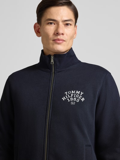 Männermodel trägt Regular Fit Sweatjacke aus Baumwoll-Mix von Tommy Hilfiger in Unifarben mit Label-Print, Reißverschluss, Stehkragen, Nahaufnahme Oberkörper.
