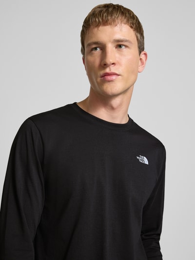 Męski model nosi Bluzka z długim rękawem z wyhaftowanym logo od The North Face, mieszanka bawełny, krój regular fit, okrągły dekolt, długość tyłu w rozmiarze M: 70 cm, kolor czarny, gładka faktura, zbliżenie na górną część ciała.