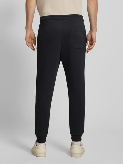 Männermodel trägt Regular Fit Sweatpants mit Steekzakken Model 'GORDON' van JACK & JONES in zwart, Materiaalmix met katoen, Achterzak, elastische band met tunnelkoord, Ganzkörperansicht Rückansicht, Heren sweatpants, Binnenbeenlengte bij maat M 70 cm.