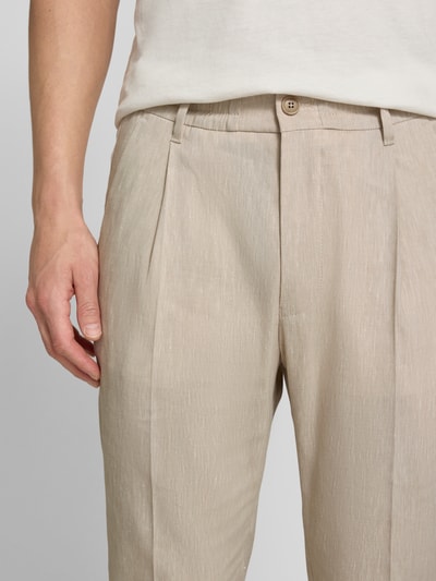 Mężczyzna nosi Hose mit Bügelfalte und elastischem Bund Modell 'CHASY' von Drykorn, beżowy len z wiskozą, krój slim fit, z przodu widok zbliżeniowy, Szerokość w rozmiarze 32/32: 44 cm, długość nogawki: 66 cm.
