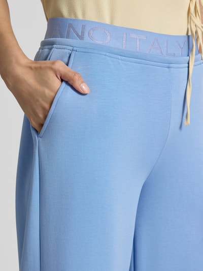 Frauenmodel trägt Sweatpants mit Stretch-Anteil von Milano Italy in Hellblau, Modal-Elasthan-Mix, Logo-Bund, Eingrifftaschen, Nahaufnahme Oberkörper.