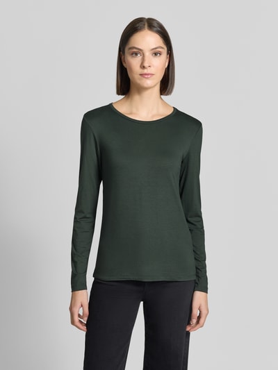 Kobiece model prezentuje bluzka z długim rękawem z mieszanki wiskozy i elastanu Model 'Liana' od FREE/QUENT, krój slim fit, okrągły dekolt, długość tyłu w rozmiarze S: 59 cm, kolor ciemnozielony, gładka faktura, pełny widok z przodu.