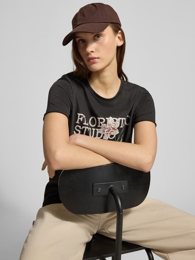 Modelka nosi Regular Fit T-Shirt aus reiner Baumwolle Modell 'LUCY' od Only, czarna bawełna, nadruk z motywem, krótki rękaw, jersey, unikatowa tekstura, widok na górną część ciała z przodu
