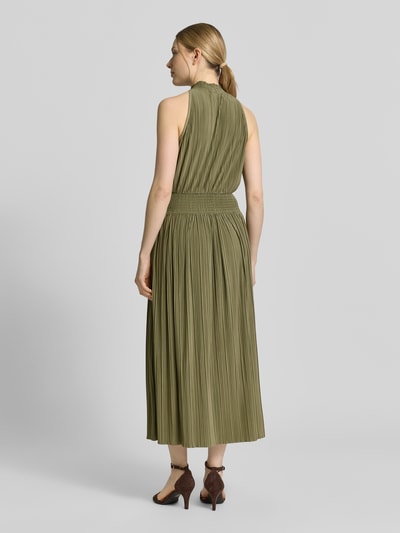 Frauenmodel trägt Plisseekleid mit Smok-Details Modell 'UMA' von Samsøe Samsøe in Olivgrün, taillierter Schnitt, Midikleid, Ganzkörperansicht Rückansicht.