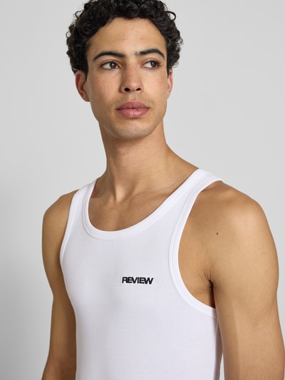 Mężczyznamodel nosi top Tanktop in Ripp-Optik mit Logo von REVIEW z bawełny, krój slim fit, efekt prążkowania, logo, okrągły dekolt, długość tyłu w rozmiarze M: 67 cm, jasny kolor, gładka tekstura, zdjęcie z bliska górnej części ciała.