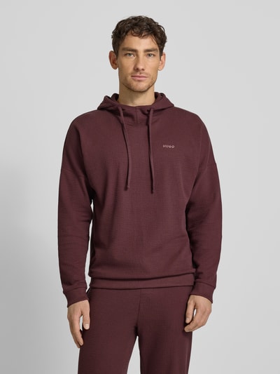 Männermodel trägt Regular Fit Hoodie aus Baumwoll-Mix Modell 'AUSTIN' von HUGO in unifarbenem Bordeaux mit Waffel-Struktur, Ganzkörperansicht von vorne.