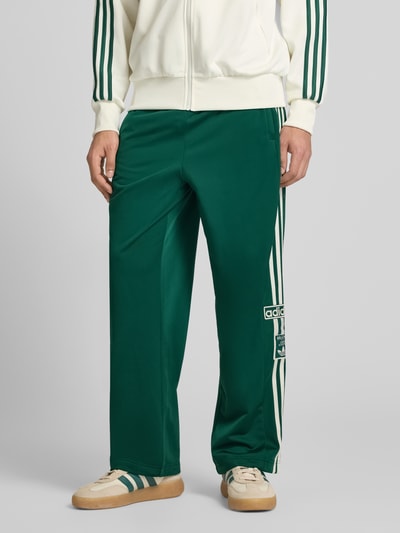 Männermodel trägt Sweatpants mit elastischem Bund Modell "ADIBREAK" von adidas Originals, grün mit weißen Streifen, Label-Stitching, Französische Eingrifftaschen, Lockerer-Schnitt, Ganzkörperansicht von vorne.