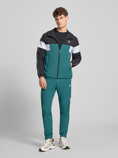 Männermodel trägt Regular Fit Jacke mit Logo-Stitching Modell 'Caspio' von SERGIO TACCHINI in Grün, Schwarz und Weiß, Ganzkörperansicht von vorne. Elastischer Material-Mix, Reißverschluss, Kapuze, Eingrifftaschen, elastische Ärmelabschlüsse, sportlicher Look.