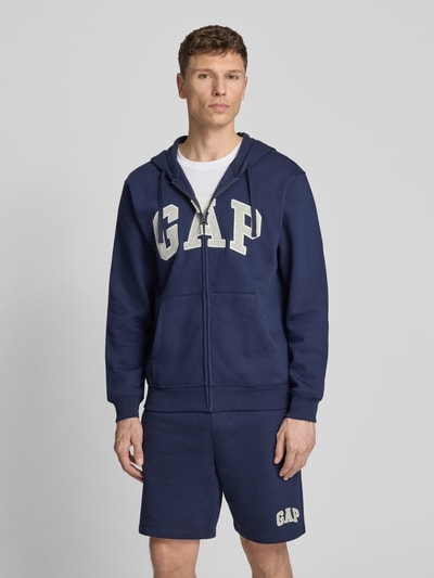 Männermodel trägt Sweatjacke mit Logo und Känguru-Tasche von GAP aus dunkelblauem Baumwoll-Mix, Regular-Fit, Ganzkörperansicht von vorne
