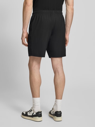 Männermodel trägt Relaxed Fit Sport-Shorts mit Logo-Stitching von Lacoste Sport, unifarben, elastischer Bund, seitliche Taschen, Ganzkörperansicht Rückansicht.