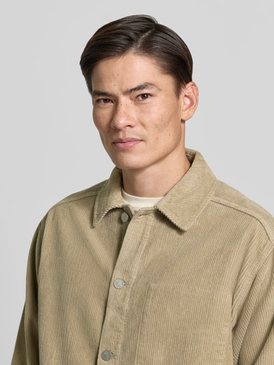 Mannenmodel draagt Relaxed Fit vrijetijdsoverhemd uit pure katoen van ARMEDANGELS, lichtbruine tint, structuur van ribstof, close-up bovenlichaam
