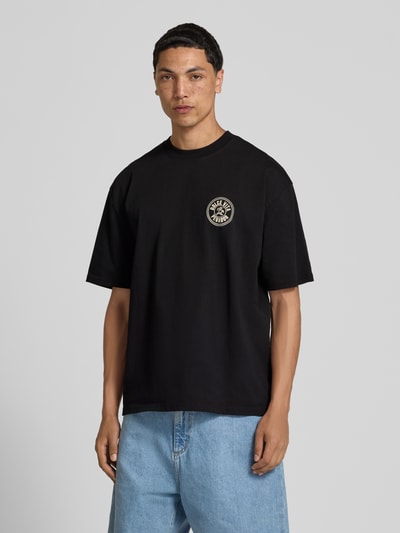 Männermodel trägt Oversized T-Shirt mit Label-Print von Pegador aus reiner Baumwolle, schwarze Farbe, Rundhalsausschnitt, Ganzkörperansicht von vorne. Rückenlänge bei Größe M: 72 cm.