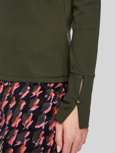 Frauenmodel trägt Longsleeve mit Stehkragen und Zierknöpfen von Marc Cain im Baumwoll-Elasthan-Mix, Nahaufnahme Oberkörper.