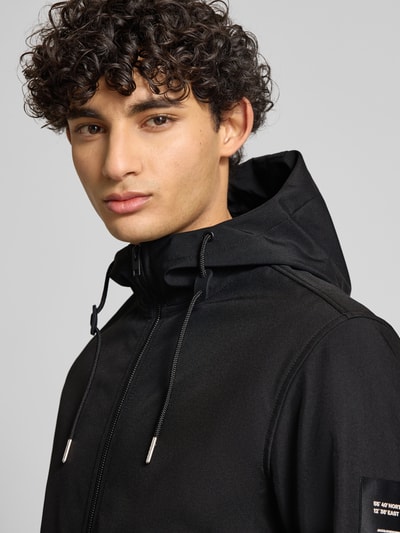 Männermodel trägt zwarte softshell-jack met capuchon en tunnelkoord, ritssluiting en ritszakken, regular fit van Jack & Jones, nahaufnahme oberkörper
