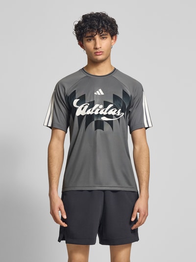 Männermodel trägt Regular Fit T-Shirt mit Label Print von adidas Sportswear, Optik: Unifarben, Kontraststreifen, Kurzarm, Ganzkörperansicht von vorne.