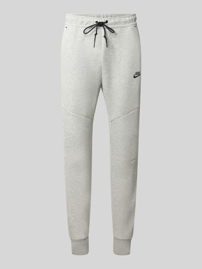 Produktfoto, Slim Fit Sweathose aus Baumwoll-Mix von Nike, hellgrau mit schwarzen Kordeln, weiche Textur auf glattem Hintergrund.